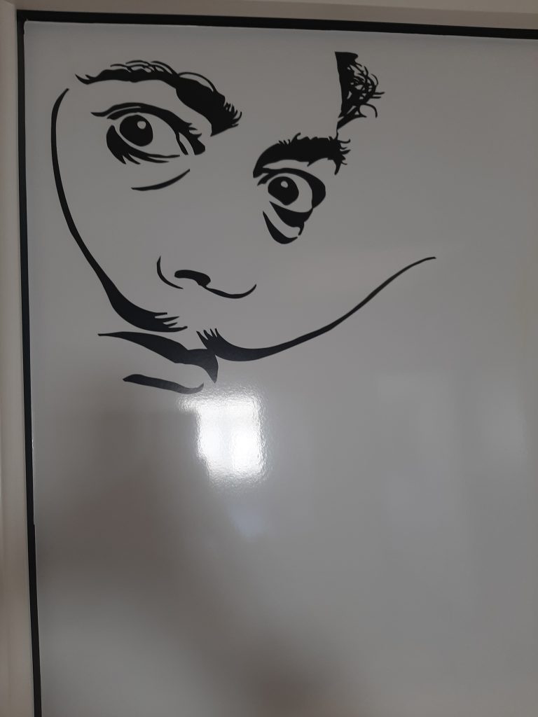 autocollant du visage de Salvador Dali avec moustache collé sur le tableau blanc de la salle de réunion